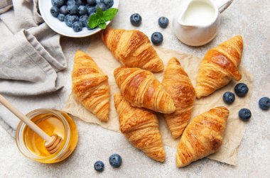 Lezzetli altın sarısı kruvasanlar yabanmersini, bal ve sütle servis edilir ve nefis bir kahvaltı hazırlar.