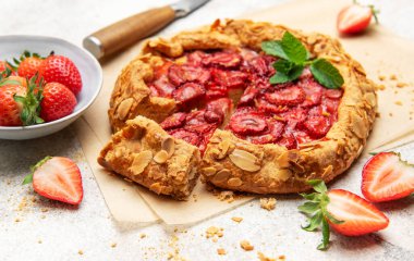 Badem gevreği ve nane yaprağı ile süslenmiş taze fırınlanmış çilek galeti, taze çilek ile servis edilir.