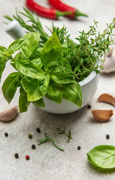 Havan ve kabuk taze fesleğen, kekik ve biberiye ile taşar, yanında da sarımsaklı karanfil, biberli ve biberli biberli mutfak masasında.