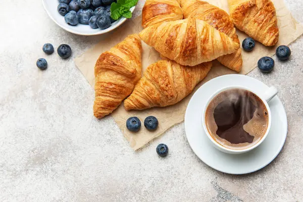 Taze pişmiş kruvasan, yabanmersini ve lezzetli bir kahvaltı hazırlayan dumanı tüten kahve.