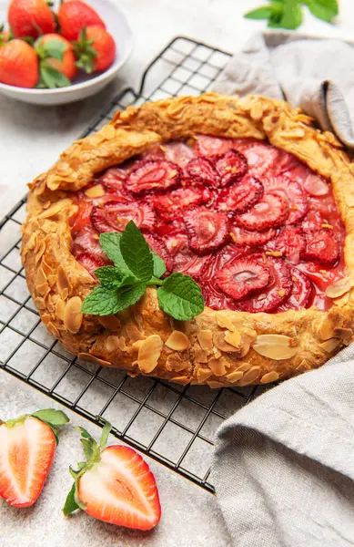 Nane yapraklarıyla süslenmiş taze pişmiş çilek galeti ve soğutma rafında duran badem gevrekleri.