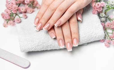 Beyaz havluda mükemmel Fransız manikürlü kadın elleri, beyaz arka planda pembe çiçekler.