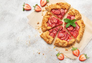 Badem gevreği ve nane yaprağı ile süslenmiş taze pişmiş çilek galeti pişirme kağıdıyla dilimleniyor.