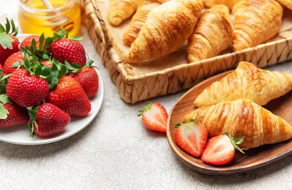 Taze pişmiş kruvasan çilek ve bal ile servis edilir, nefis bir kahvaltı hazırlar.