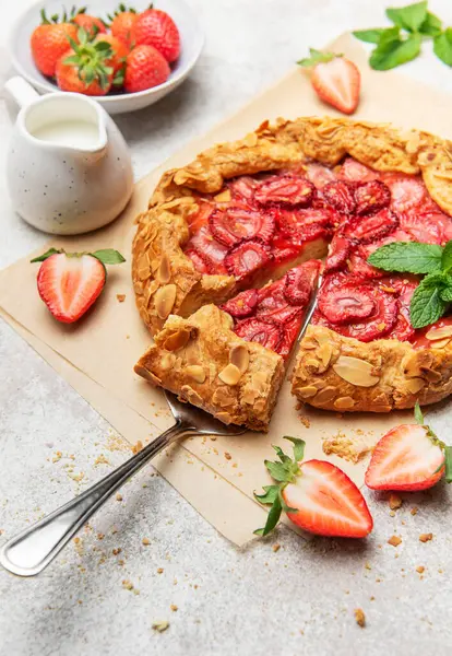 Badem yaprakları ve nane yapraklarıyla süslenmiş taze fırınlanmış çilek galeti, yakınlardaki taze çileklerle parşömen kağıdında dinleniyor.