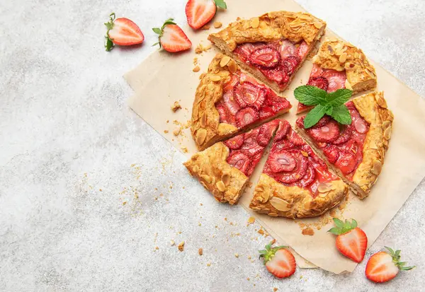 Badem gevreği ve nane yaprağı ile süslenmiş taze pişmiş çilek galeti pişirme kağıdıyla dilimleniyor.