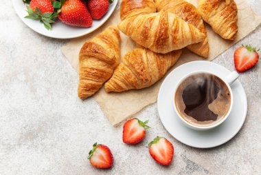 Taze pişmiş kruvasan, bir fincan dumanı tüten kahve ve nefis bir kahvaltı sahnesi yaratan sulu çilekler.