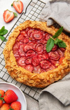 Badem gevreği ve nane yapraklarıyla süslenmiş taze pişmiş çilek galeti, tel askıda soğutuluyor.