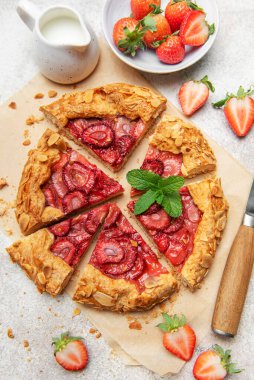 Badem gevreği ve nane yaprağı ile süslenmiş taze pişmiş çilek galeti pişirme kağıdıyla dilimleniyor.