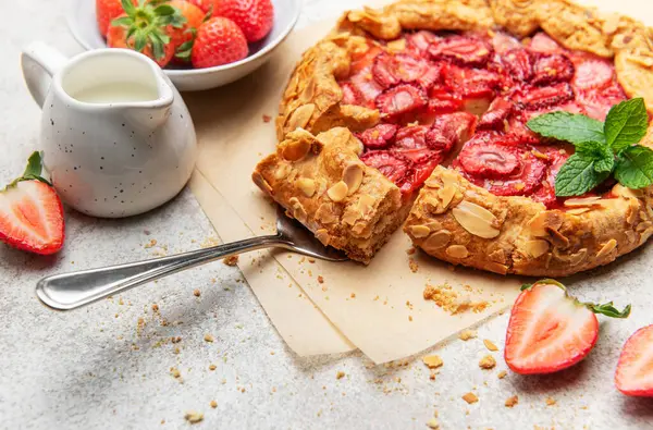 Badem yaprakları ve nane yapraklarıyla süslenmiş taze fırınlanmış çilek galeti, yakınlardaki taze çileklerle parşömen kağıdında dinleniyor.