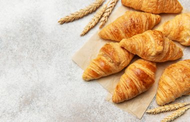 Kurabiye kağıdına yerleştirilmiş altın sarısı kruvasanlar, buğdayla birlikte, cazip bir fırın sahnesi yaratıyor.