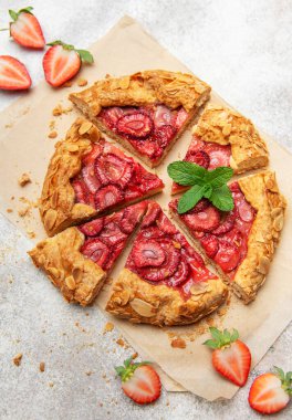 Badem gevreği ve nane yaprağı ile süslenmiş taze pişmiş çilek galeti pişirme kağıdıyla dilimleniyor.