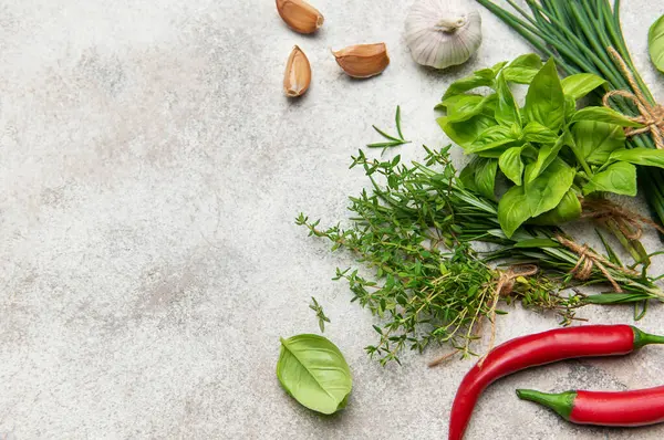 Gri arka planda taze toplanmış otlar ve baharatlar canlı bir mutfak malzemesi gösterisi yaratıyor.