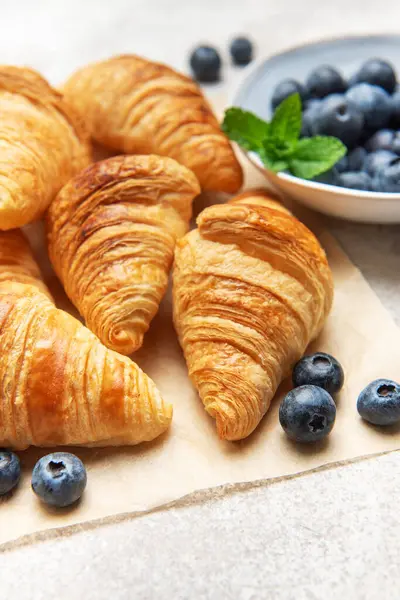 Taze pişmiş altın sarısı kruvasanlara olgun yaban mersinleri eşlik eder ve cezbedici bir kahvaltı sahnesi yaratır.