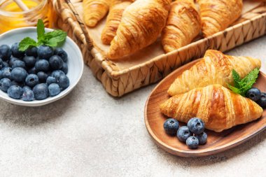 Taze pişmiş kruvasan, yaban mersini, nane yaprağı ve bal ile servis edilir ahşap tabakta lezzetli bir kahvaltı sahnesi yaratır.