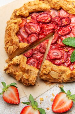 Badem yaprakları ve nane yapraklarıyla süslenmiş taze fırınlanmış çilek galeti, yakınlardaki taze çileklerle parşömen kağıdında dinleniyor.