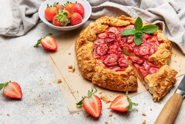 Badem yaprakları ve nane yapraklarıyla süslenmiş taze fırınlanmış çilek galeti, yakınlardaki taze çileklerle parşömen kağıdında dinleniyor.