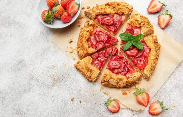 Badem gevreği ve nane yaprağı ile süslenmiş taze pişmiş çilek galeti pişirme kağıdıyla dilimleniyor.