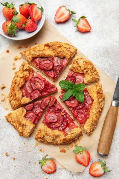 Badem gevreği ve nane yaprağı ile süslenmiş taze pişmiş çilek galeti pişirme kağıdıyla dilimleniyor.