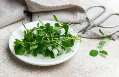 Taze bezelyeler beyaz bir tabakta makas ve desenli bir arka planda keten peçeteyle filizlenir.