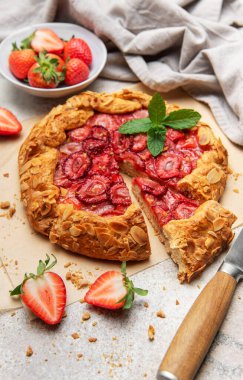 Badem yaprakları ve nane yapraklarıyla süslenmiş taze fırınlanmış çilek galeti, yakınlardaki taze çileklerle parşömen kağıdında dinleniyor.