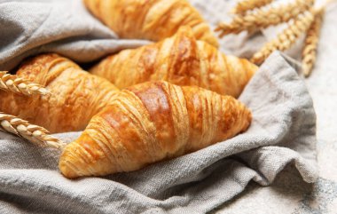 Altın sarısı kruvasanlar ve buğday sapları keten kumaş üzerinde samimi bir kahvaltı sahnesi yaratır.
