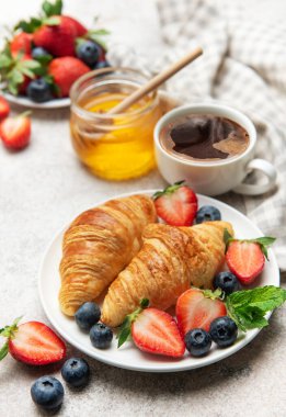 Lezzetli bir kahvaltı için taze kruvasanlarla sulu çilek, yabanmersini, nane yaprağı, bir fincan kahve ve bal servis edilir.
