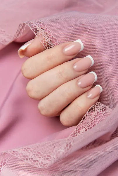 Pembe arka planda dantelli Fransız manikürünü gösteren bir kadın.
