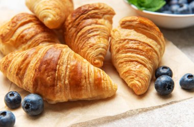 Taze pişmiş altın sarısı kruvasanlara olgun yaban mersinleri eşlik eder ve cezbedici bir kahvaltı sahnesi yaratır.