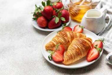 Taze pişmiş kruvasan, sulu çilek ve bal ile servis edilip nefis bir kahvaltı deneyimi yaratıyor.