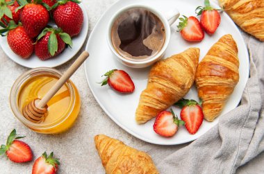 Taze pişmiş kruvasan, sulu çilek ve bir fincan kahve bir kavanoz bal ile tamamlanmış enfes bir kahvaltı sahnesi yaratır.