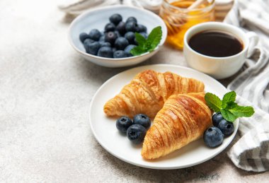 Lezzetli bir kahvaltı hazırlayan taze pişmiş kruvasan, yabanmersini, bal ve kahve ile servis edilir.