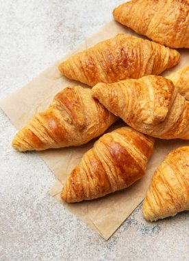 Kurabiye kağıdına yerleştirilmiş altın sarısı kruvasanlar, buğdayla birlikte, cazip bir fırın sahnesi yaratıyor.