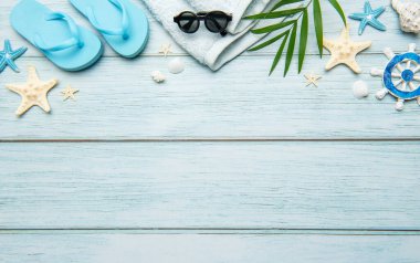 Terlikler, güneş gözlükleri, havlu, deniz kabukları, denizyıldızı ve gemi tekerleği açık mavi ahşap arka planda fotokopi alanı olan bir çerçeve oluşturuyor.