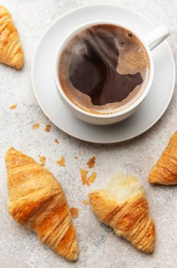 Altın rengi kruvasan ve dumanı tüten bir fincan kahve dokulu bir yüzey üzerinde cezbedici bir kahvaltı sahnesi yaratır.