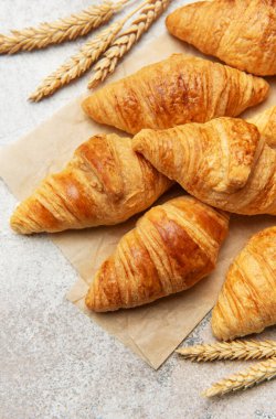 Kurabiye kağıdına yerleştirilmiş altın sarısı kruvasanlar, buğdayla birlikte, cazip bir fırın sahnesi yaratıyor.