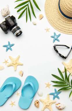 Yaz aksesuarları beyaz arkaplanda kamera, parmak arası terlik, güneş gözlüğü, hasır şapka, denizyıldızı ve deniz kabukları da dahil olmak üzere bir çerçeve oluşturuyor.