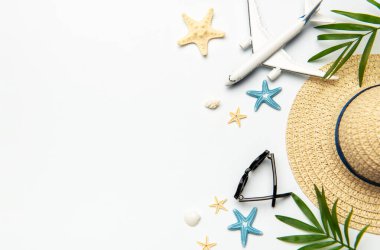 Yaz tatili aksesuarları uçak, güneş gözlüğü, hasır şapka, deniz kabuğu, deniz yıldızı ve palmiye yaprakları gibi beyaz arka planda bir seyahat kavramı yaratır.