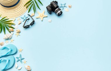 Terlik, güneş gözlüğü, kamera, deniz kabuğu, denizyıldızı ve hasır şapka gibi plaj aksesuarları açık mavi arka planda fotokopi alanı olan bir çerçeve oluşturuyorlar.