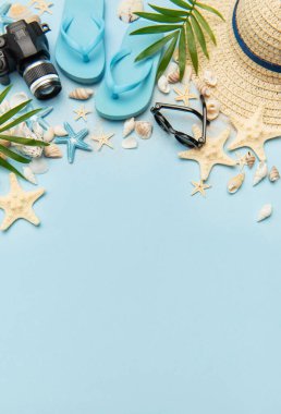 Deniz kabukları, güneş gözlükleri, denizyıldızları, parmak arası terlikler, kamera ve hasır şapka açık mavi arkaplanda fotokopi alanı olan bir çerçeve oluşturuyorlar.