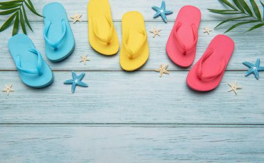 Titrek parmak arası terlikler ve deniz yıldızı eskimiş mavi ahşap bir yüzeye dizilmiş. Rahatlatıcı bir yaz kaçamağının özünü çağrıştırıyor.