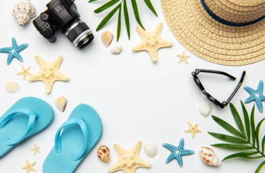 Yaz aksesuarları beyaz arkaplanda kamera, parmak arası terlik, güneş gözlüğü, hasır şapka, denizyıldızı ve deniz kabukları da dahil olmak üzere bir çerçeve oluşturuyor.