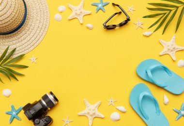 Parmak arası terlikler, güneş gözlükleri, kamera, deniz kabukları, denizyıldızı gibi yaz aksesuarları ve fotokopi alanı ile canlı sarı arkaplanı çerçeveleyen bir hasır şapka, seyahat planlama için mükemmel bir zemin oluşturur.