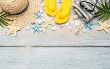 Parmak arası terlik, güneş gözlüğü, hasır şapka, deniz kabuğu ve yıldızbalığı gibi plaj aksesuarları ahşap arka planda kumla düzenlenmiş, fotokopi alanı olan bir çerçeve yaratıyor.
