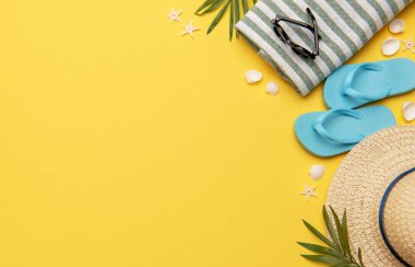 Terlik, güneş gözlüğü, hasır şapka ve havlu gibi sarı arkaplanda fotokopi alanı olan plaj aksesuarları.