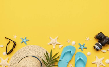 Parmak arası terlik, güneş gözlüğü, hasır şapka, deniz kabuğu, deniz yıldızı ve fotoğraf makinesi gibi plaj aksesuarları yazı geçirmek için canlı sarı bir zemin üzerinde uzanıyordu.