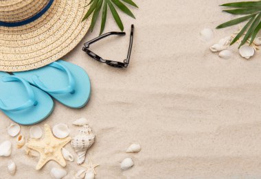 Parmak arası terlik, güneş gözlüğü ve hasır şapka gibi yaz aksesuarları deniz kabukları ve deniz yıldızlarıyla beyaz kumlarda yatmaktadır.