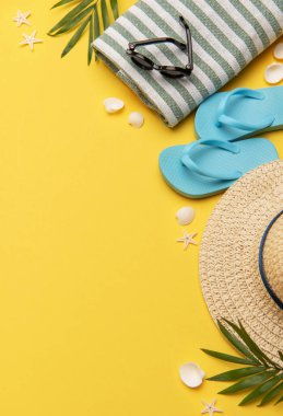 Terlik, güneş gözlüğü, hasır şapka ve havlu gibi sarı arkaplanda fotokopi alanı olan plaj aksesuarları.