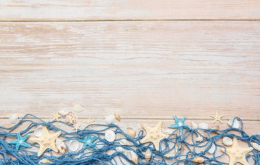 Dekoratif balık ağları, deniz yıldızları ve deniz kabuklarıyla beyaz ahşap tahtalar üzerinde yaz tatili sınırı oluşturuyorlar.