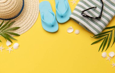 Terlik, güneş gözlüğü, hasır şapka ve havlu gibi sarı arkaplanda fotokopi alanı olan plaj aksesuarları.